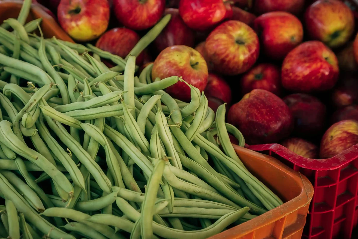 An image of green beans and apples in baskets at a supermarket
