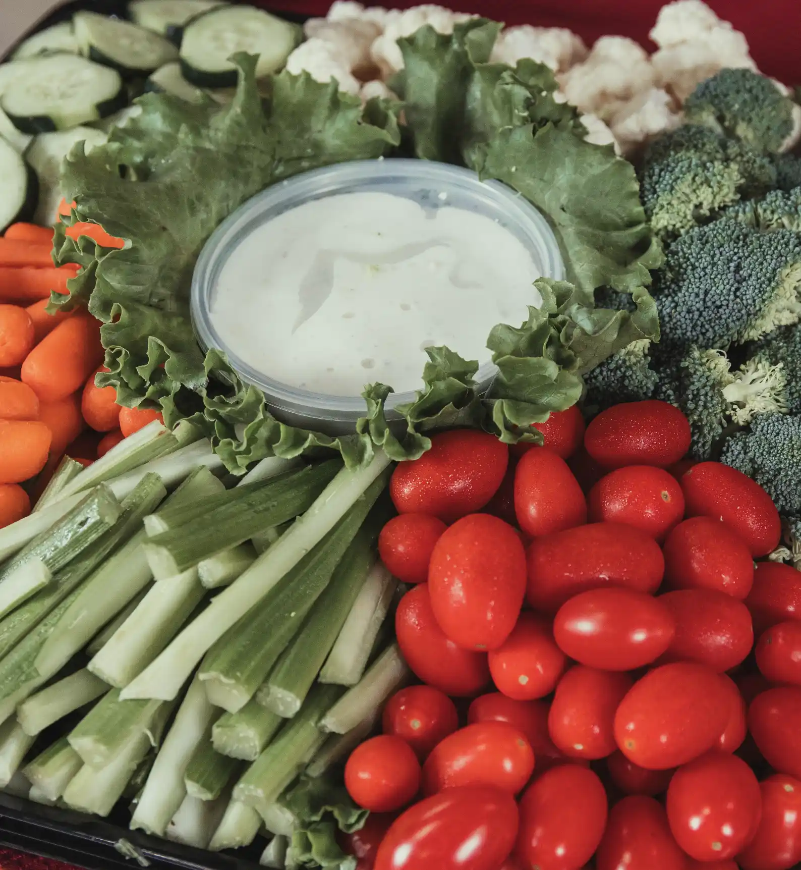 celery, carrots, cherry tomato, cucumber and broccoli arranged around a dip